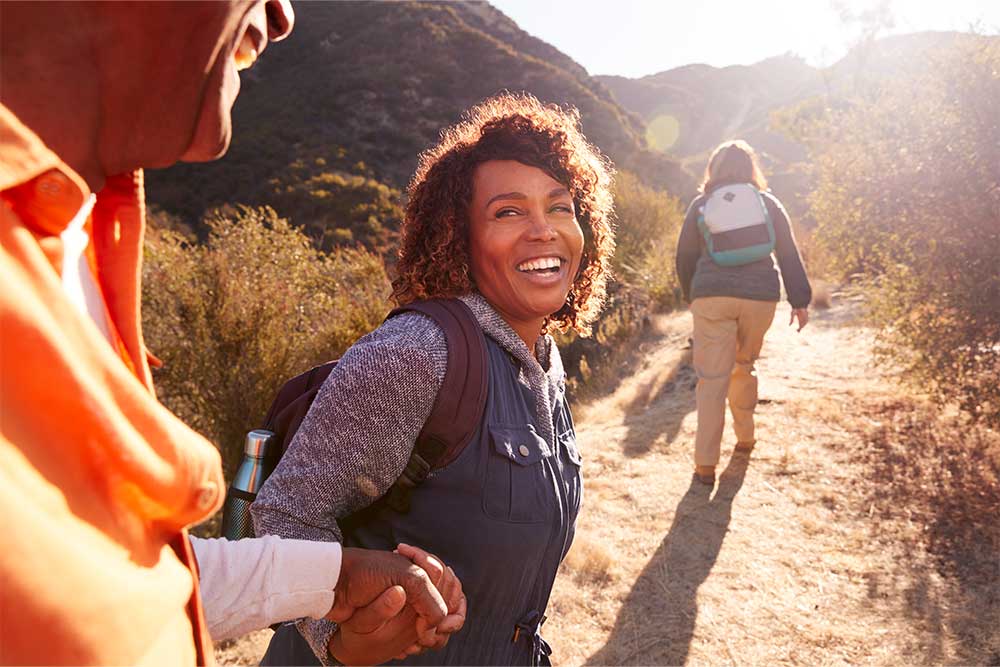 A laughing woman lends a hand while enjoying a hike with friends. Lives return to normal after living liver donation.
