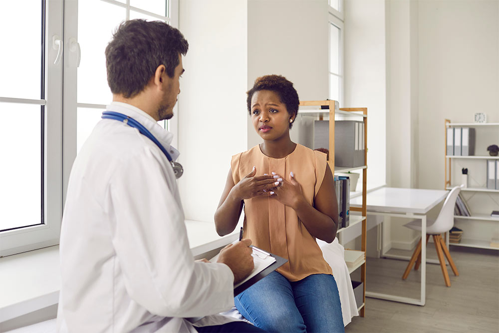 A young female patient sits in exam room and talks to a doctor about medical advice.